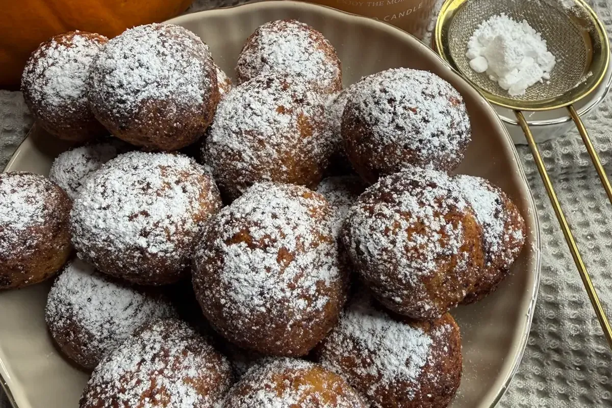 Pączki twarogowe oprószone cukrem pudrem na talerzu, w tle dynia i świeczka